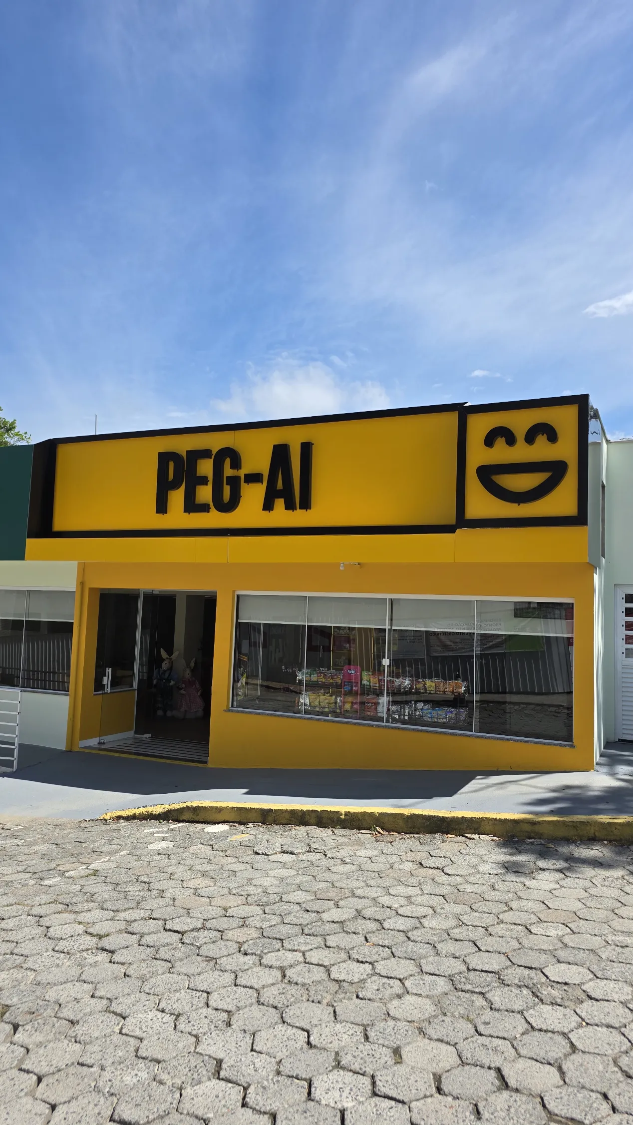 Fachada da loja PEG-AI urbana, amarela com letreiro grande, operação em regime híbrido